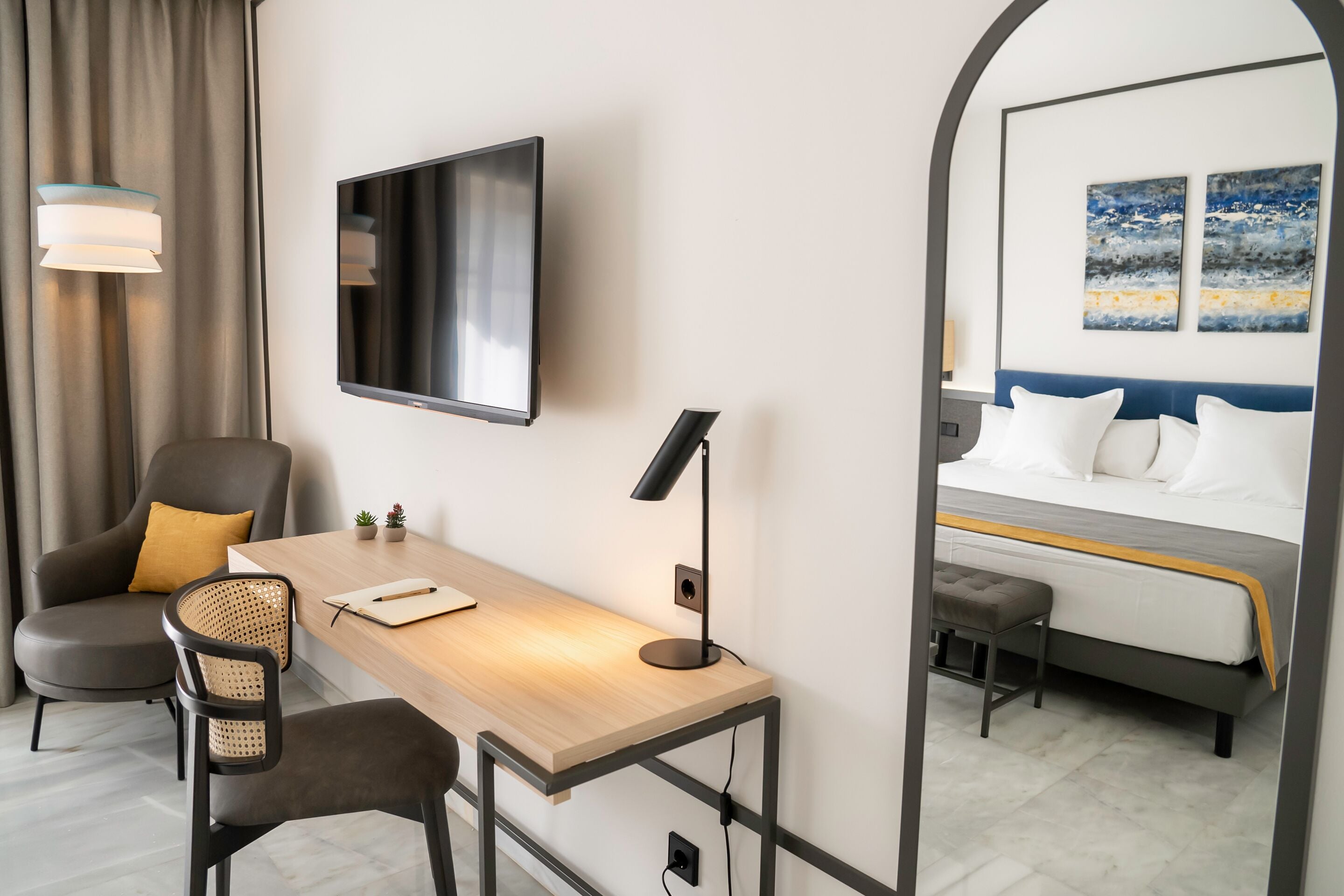 Una habitación de hotel con escritorio, dos sillas, televisor, cama y espejo.