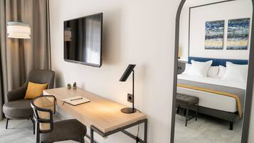 Una habitación de hotel con escritorio, dos sillas, televisor, cama y espejo.