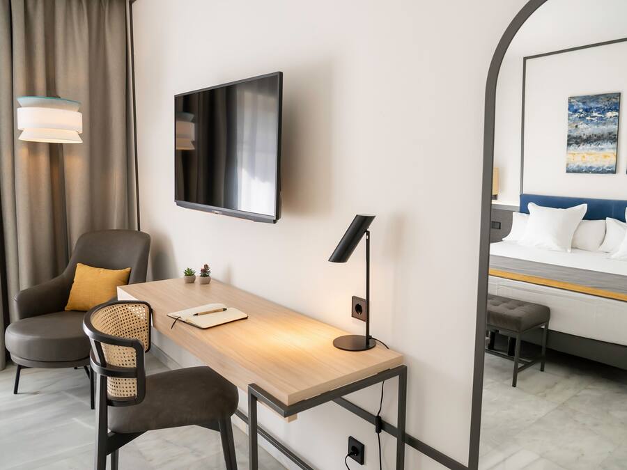 Hotellihuone, jossa on työpöytä, kaksi tuolia, televisio, sänky ja peili.