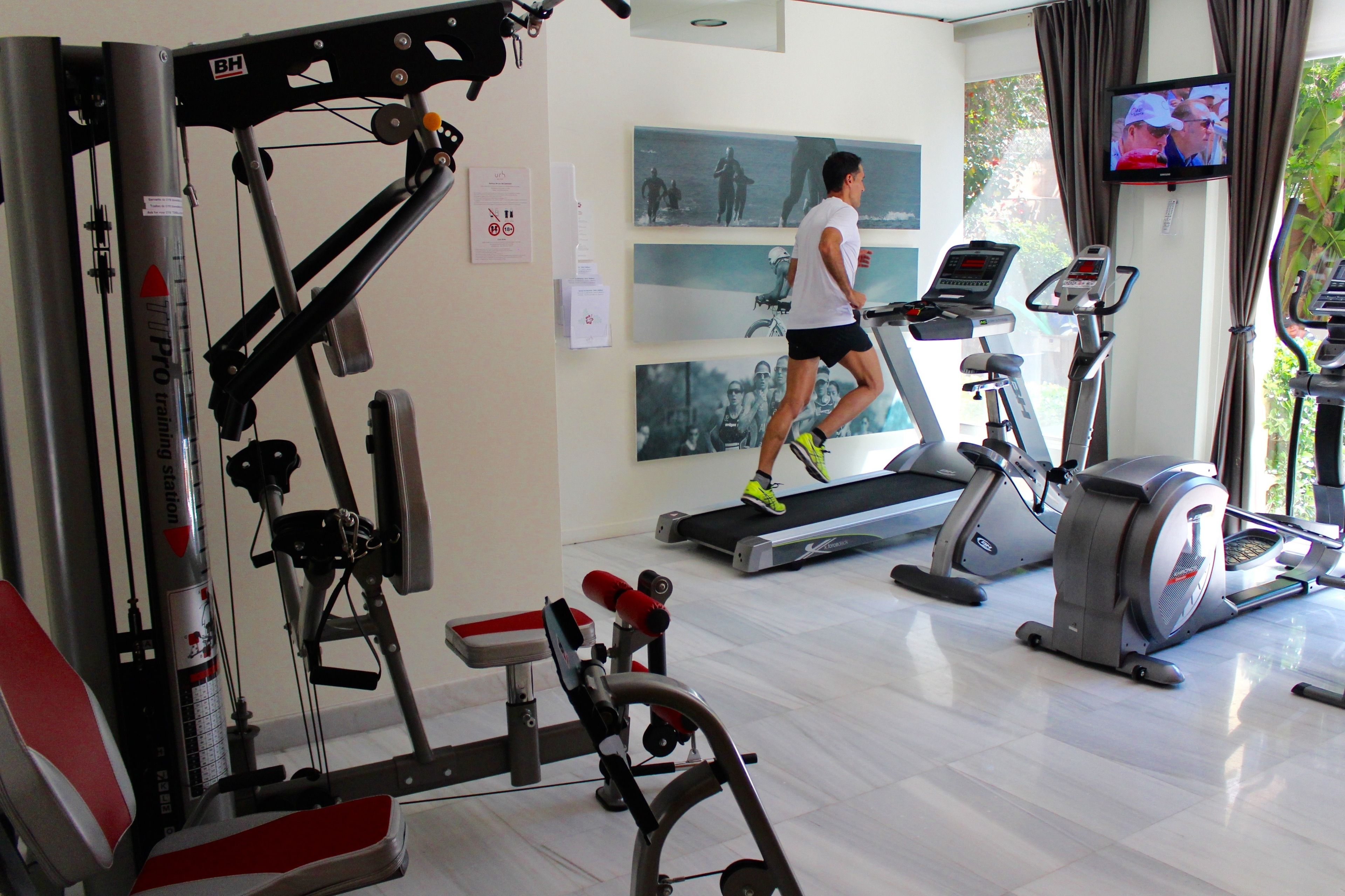 A gym with treadmills, weight machines, and a TV on the wall.