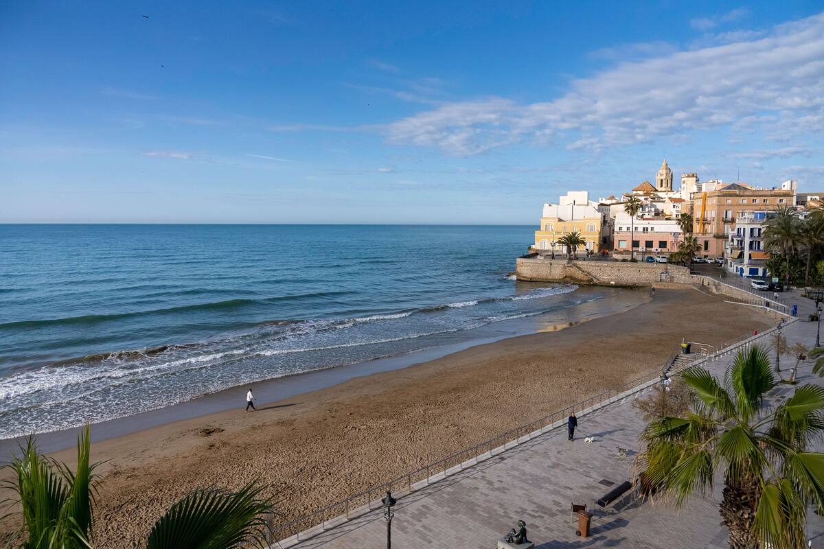 A coastal promenade with a sandy beach, a stone wall, and buildings with balconies.