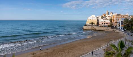 A coastal promenade with a sandy beach, a stone wall, and buildings with balconies.