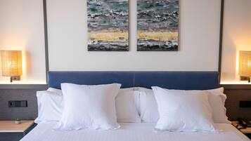 A hotel room with a large bed, white pillows, two abstract paintings on the wall, and bedside lamps.