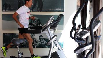 Een fitnessruimte met loopbanden en trainingsapparatuur, een muur met motiverende posters, en een raam met gordijnen.