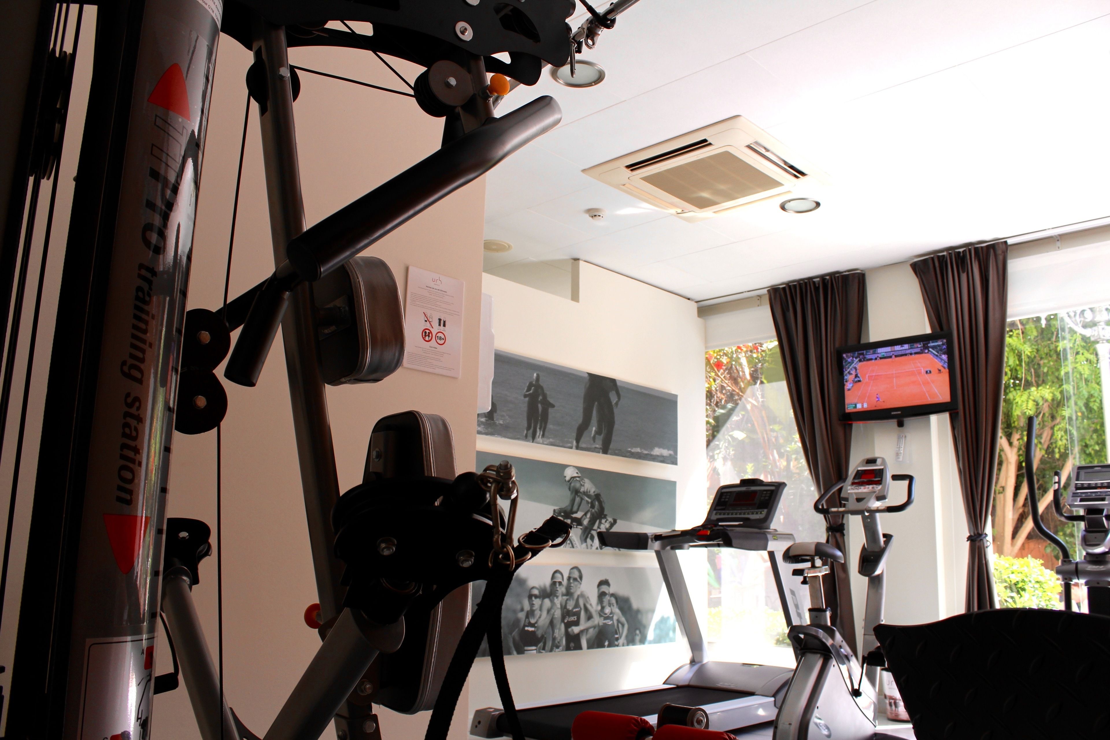 A gym with exercise equipment, a treadmill, and a television on the wall.