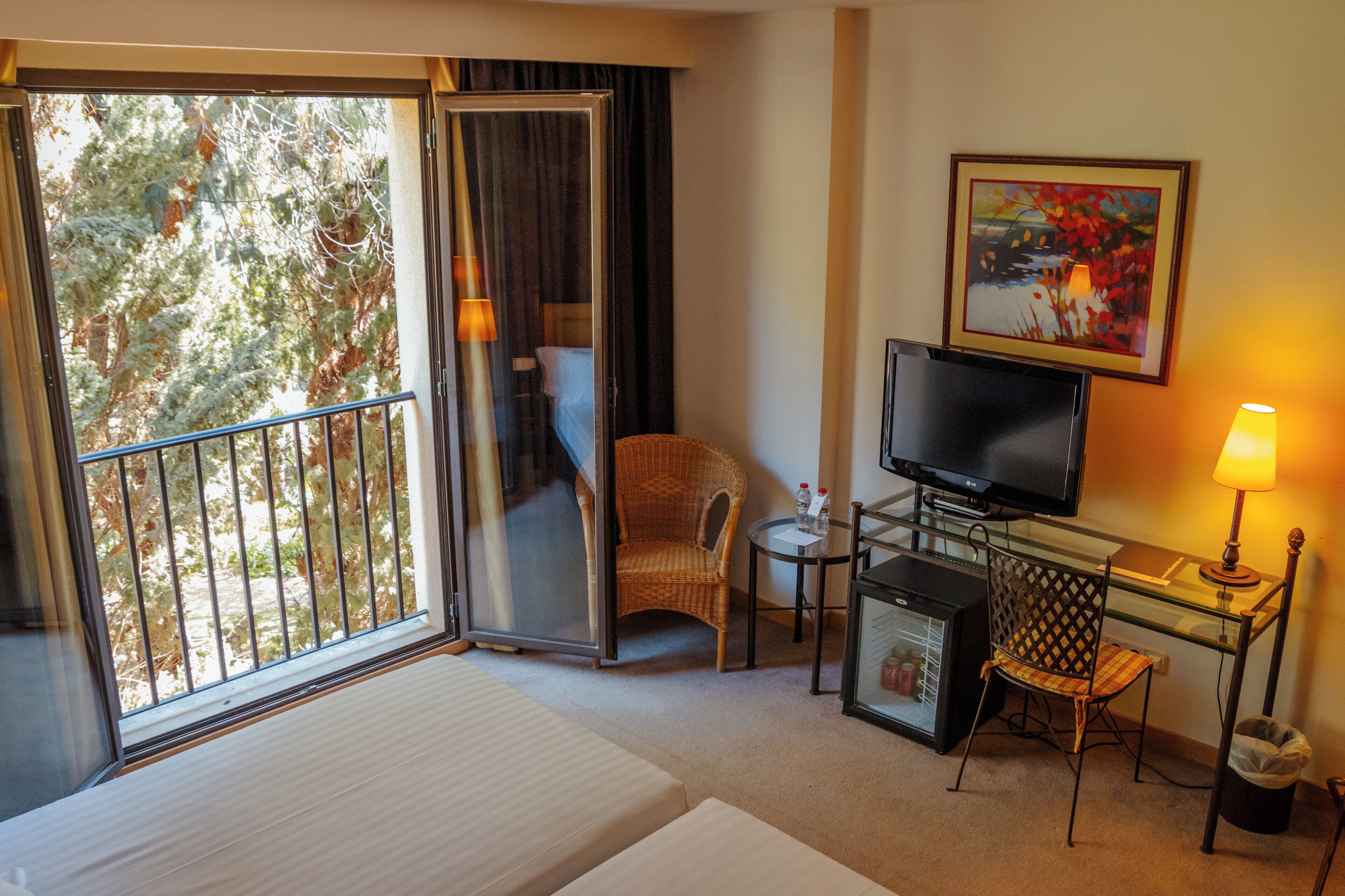 A hotel room with a bed, a television, a desk with a lamp, a chair, and a small refrigerator.