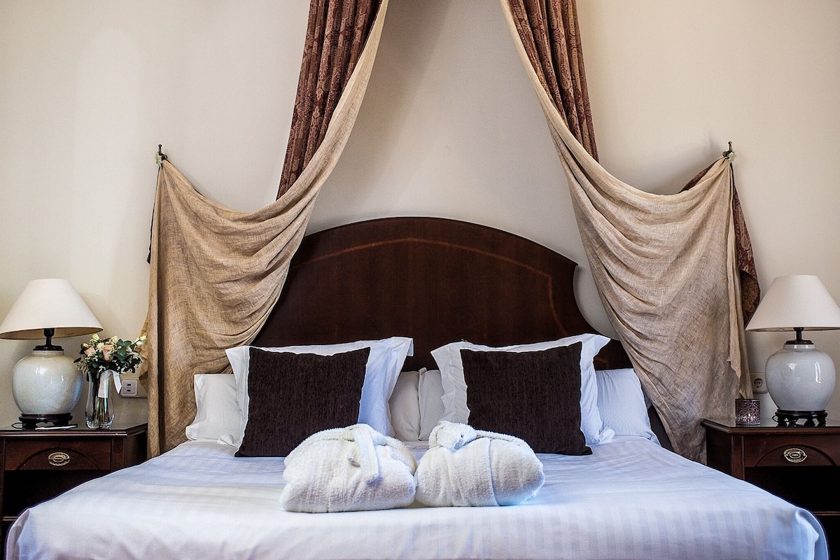 A neatly made bed with a wooden headboard, two bedside tables with lamps, and a vase with flowers on one table.