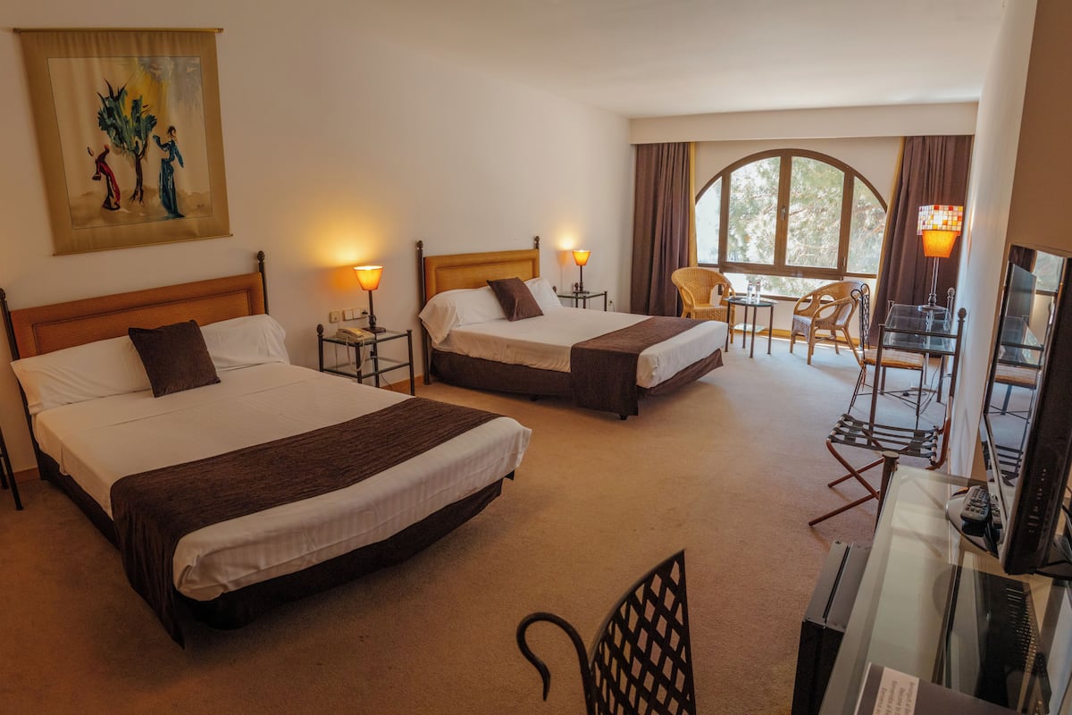 A hotel room with two beds, a desk with a chair, a TV, and a window with curtains.