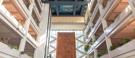 Un atrium à plusieurs niveaux, doté d’une colonne centrale en briques, de balcons ornés de plantes et d’un plafond décoré de motifs nuageux.