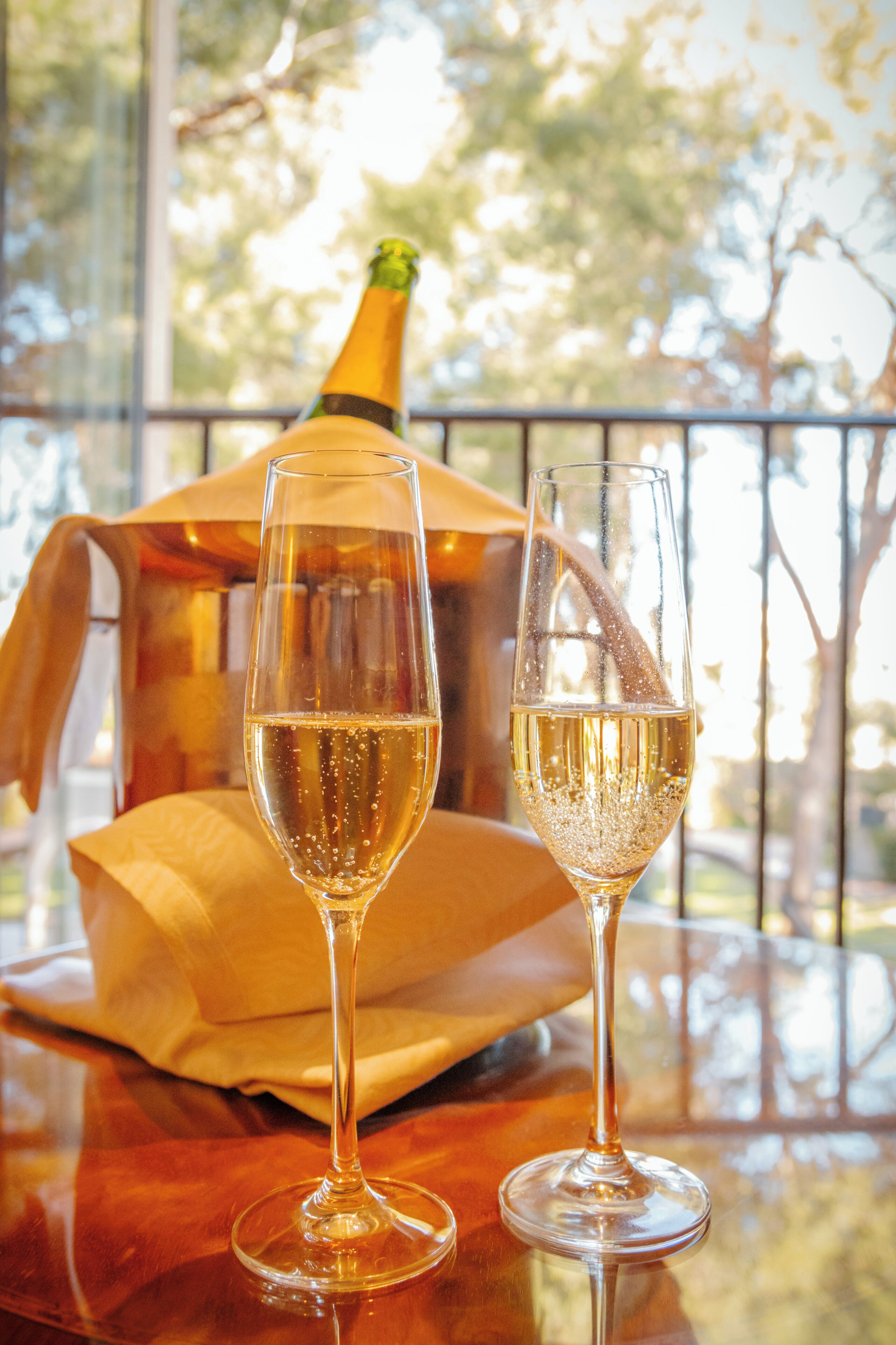Two champagne flutes on a reflective surface with a bottle and a napkin in the background.