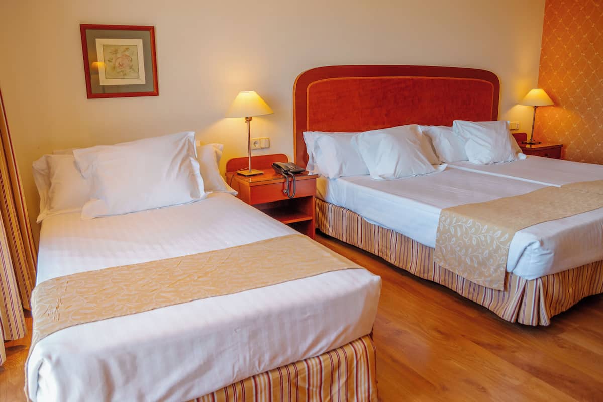 A hotel room with two beds, each with white linens and striped bed skirts. There are bedside tables with lamps and a framed picture on the wall.