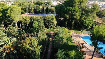 A landscaped area with a swimming pool, palm trees, and a distant view of a town.