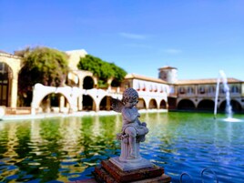 A statue of an angel on a pedestal by a fountain in a courtyard with arches and a building in the background.