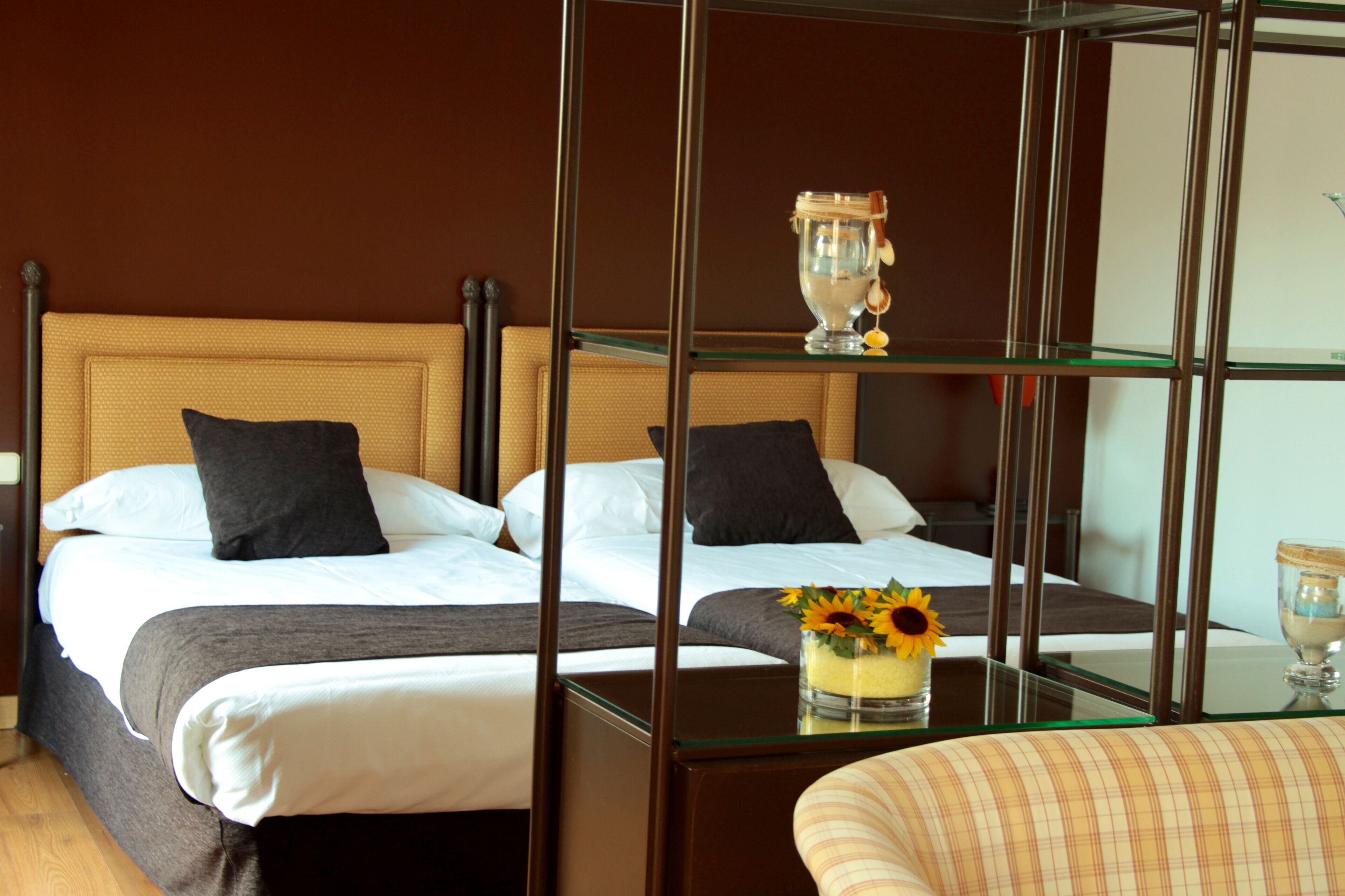 Habitación de hotel con dos camas, una mesita de vidrio, un jarrón con flores y un vaso de agua.