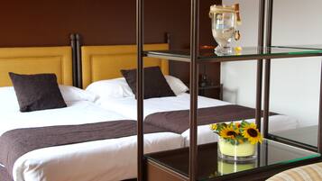 Habitación de hotel con dos camas, una mesita de vidrio con un jarrón de girasoles y un espejo enmarco.