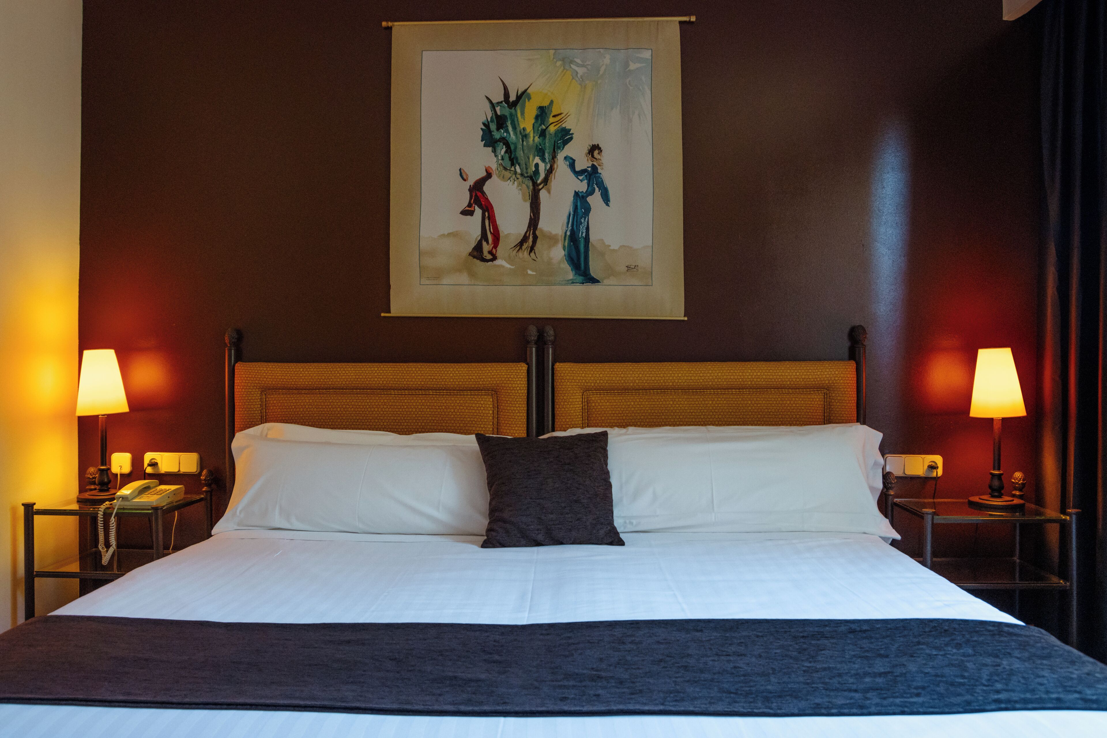 Una camera d'albergo con un letto grande, due comodini con lampade, un quadro appeso alla parete e una testata del letto in legno.