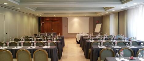 Une salle de conférence avec des rangées de tables, de chaises et des bouteilles d’eau.