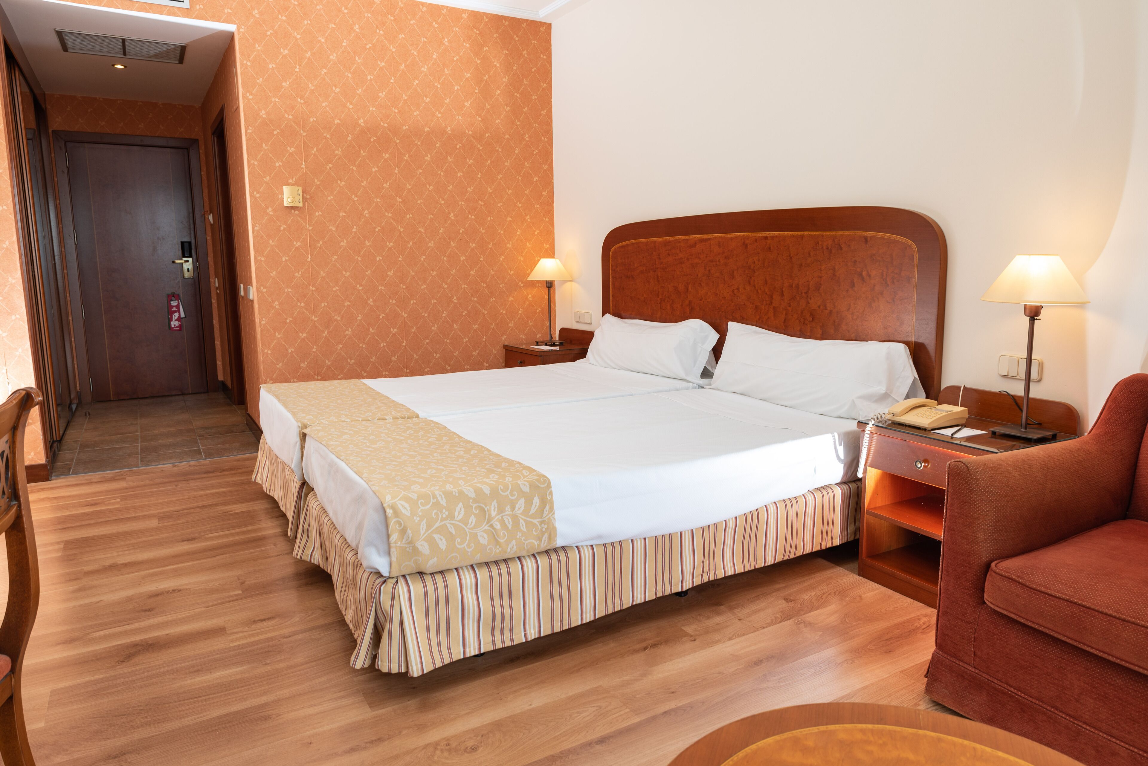 Una habitación de hotel con una cama grande, dos mesitas de noche con lámparas, suelo de madera y una pared con diseño.