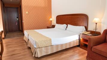 Una habitación de hotel con una cama grande, dos mesitas de noche con lámparas, suelo de madera y una pared con diseño.