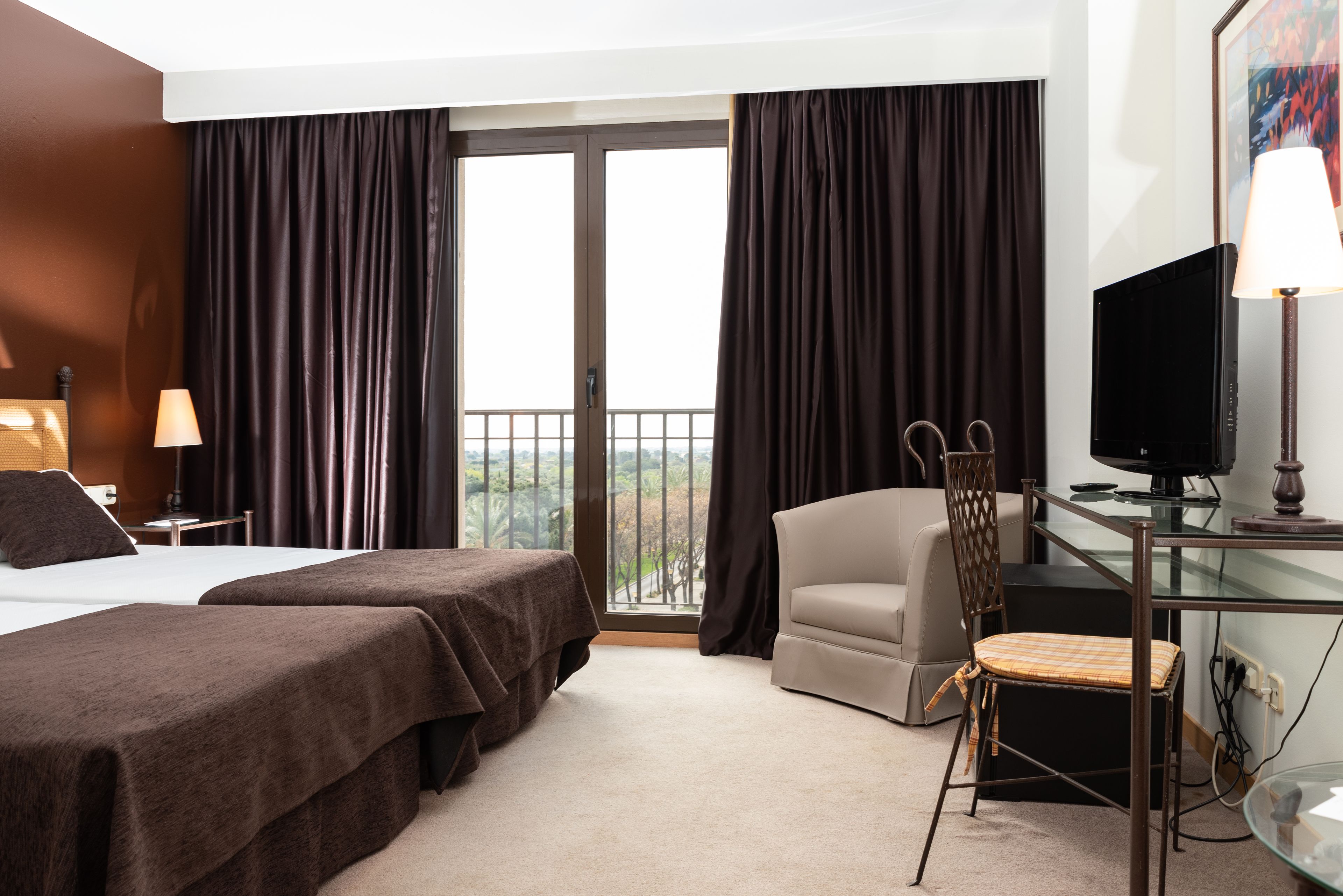 Et hotelværelse med to senge, et skrivebord med en computer, en stol og et fjernsyn.