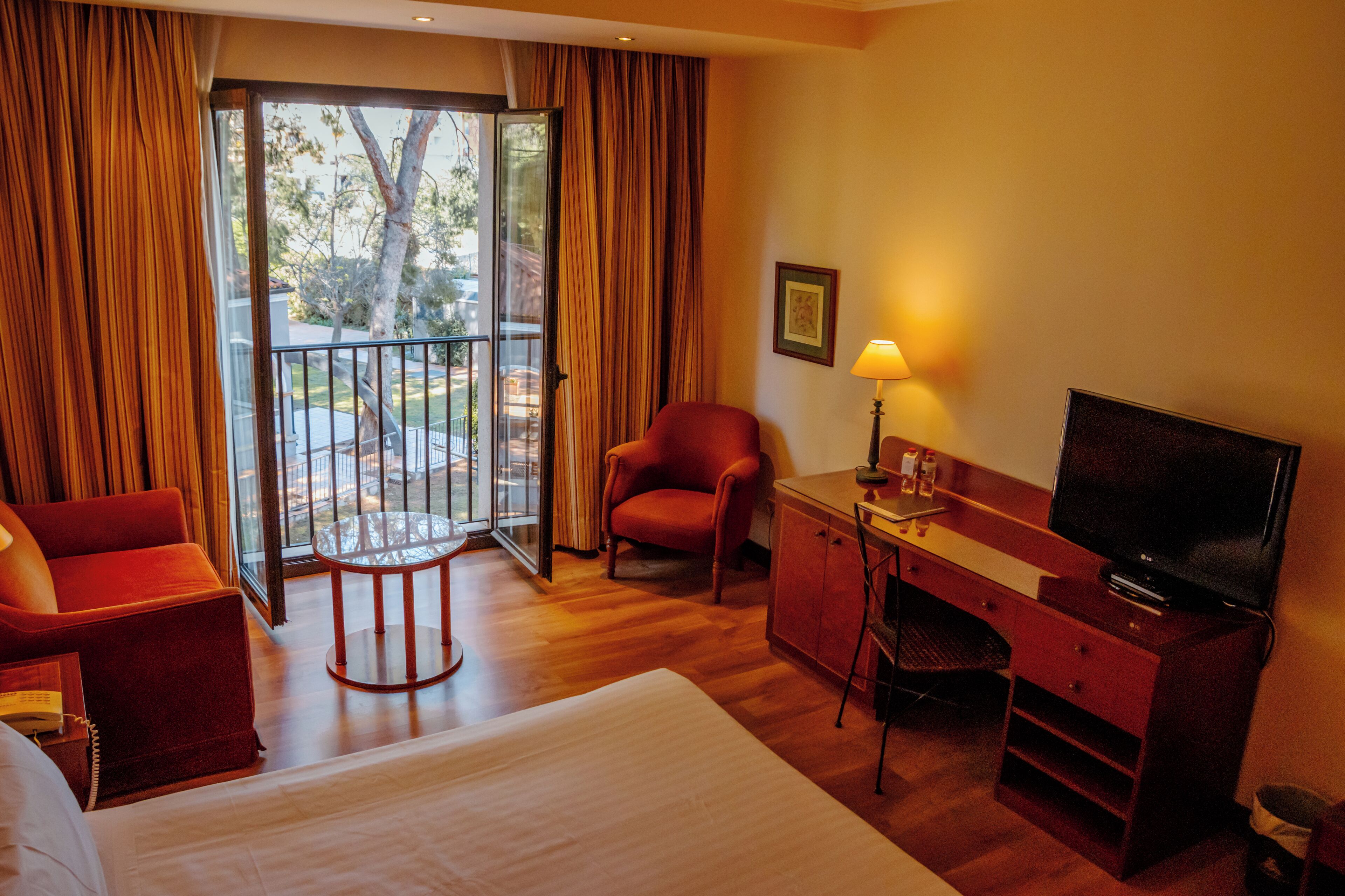 Habitación de hotel con cama, escritorio, televisor, silla y vista al exterior a través de un ventanal.