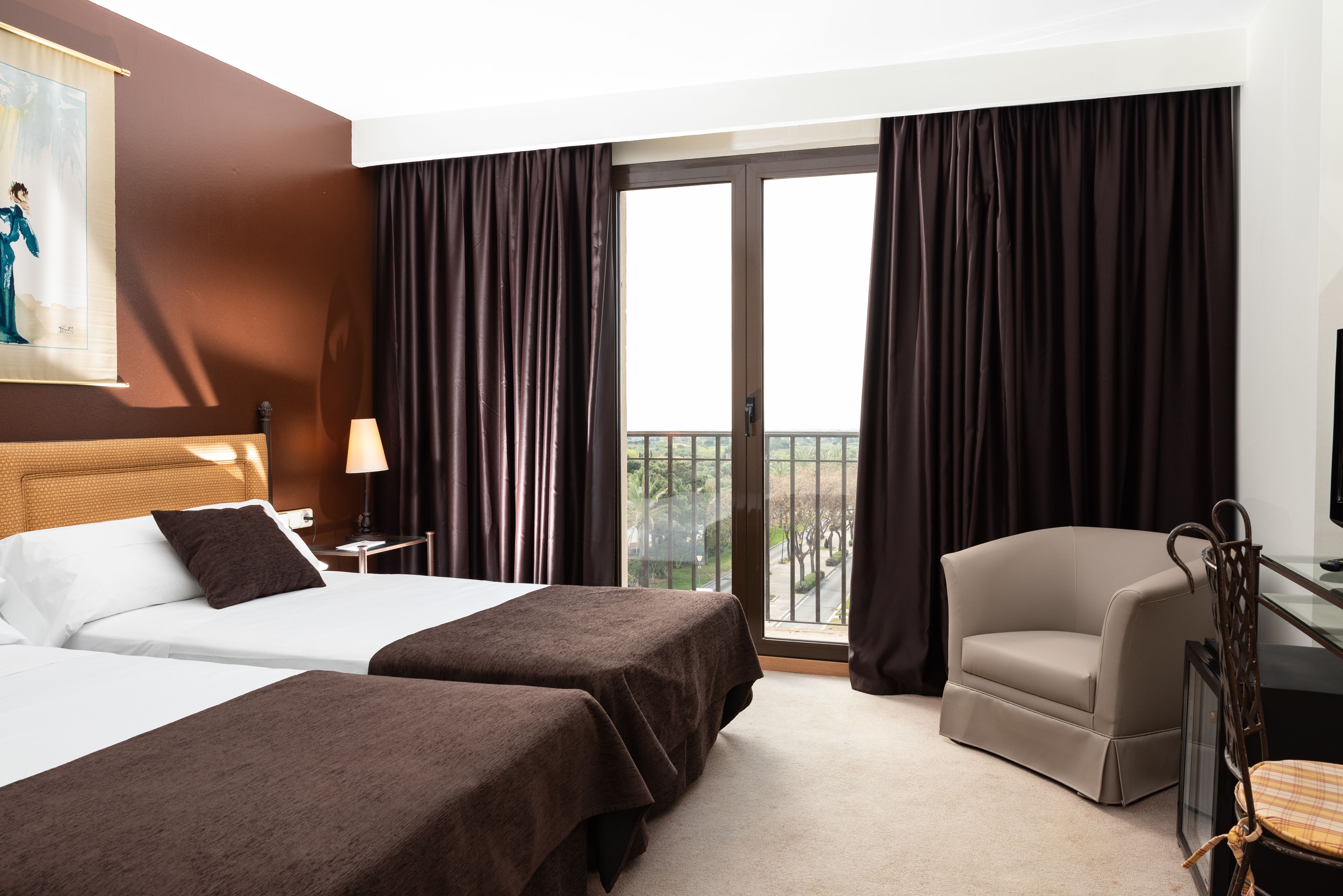 Habitación de hotel con dos camas, una silla, un escritorio y un ventanal con cortinas.
