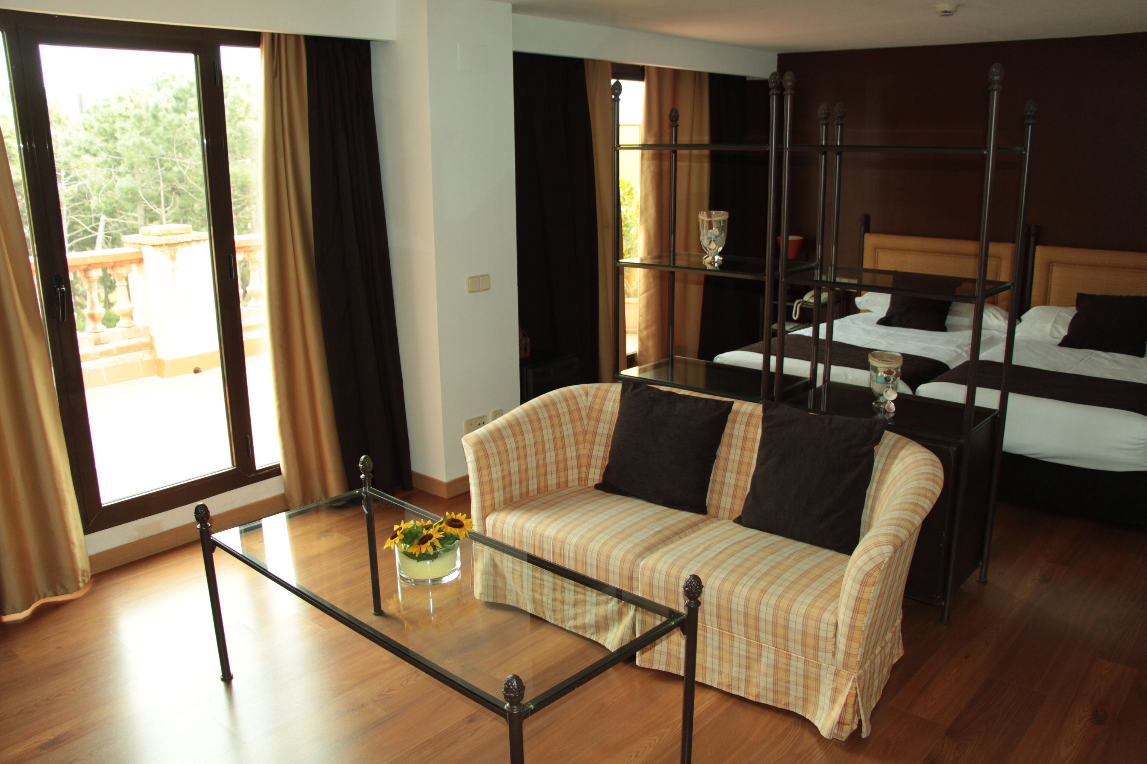 Une chambre d’hôtel avec un canapé, une table basse en verre, un lit à baldaquin et un balcon avec des rideaux.