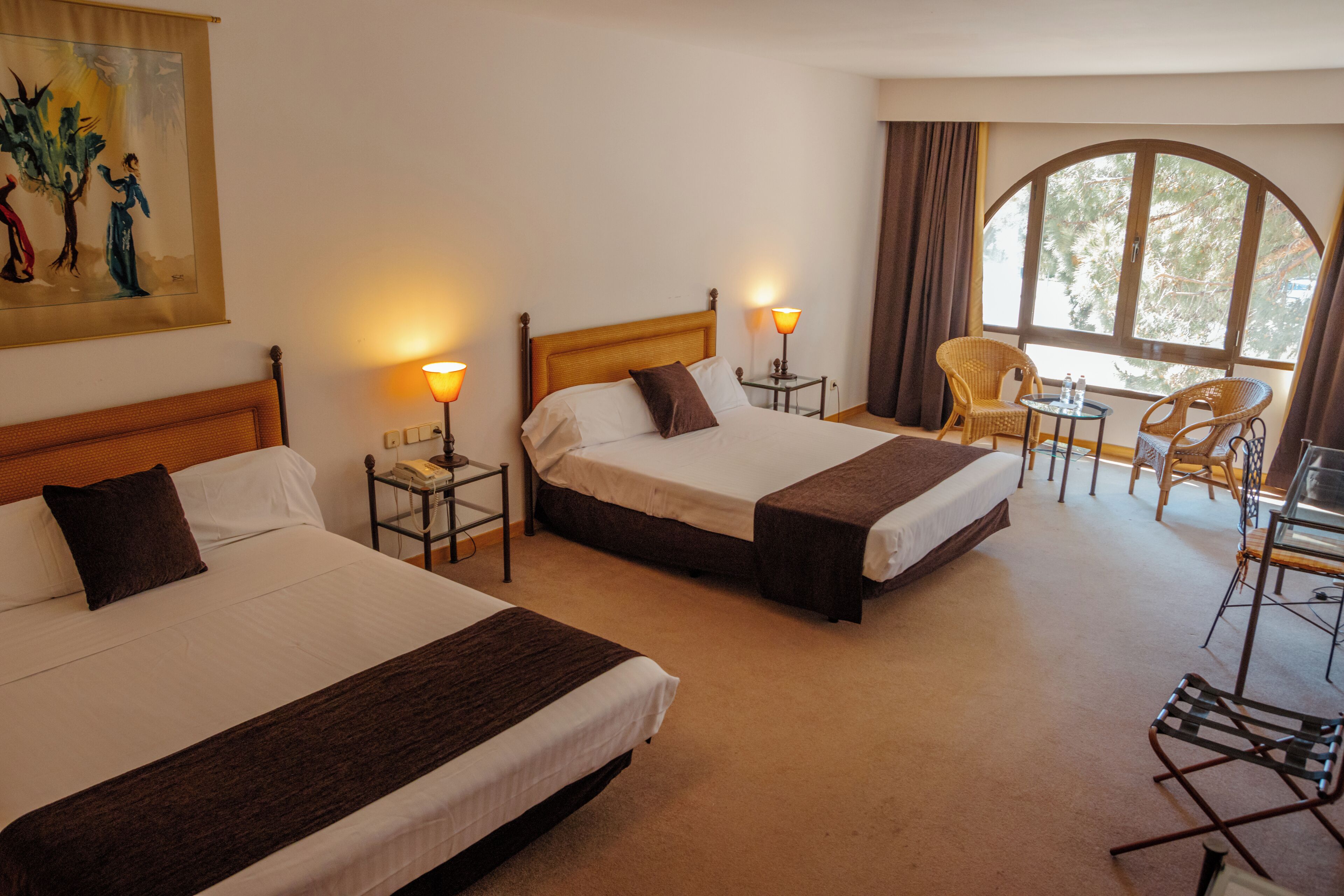 A hotel room with two beds, a small table, chairs, and a large window.
