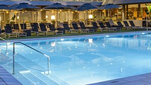 A modern hotel pool area with lounge chairs and umbrellas, a glass barrier, and a well-lit interior. - Hotel Astari (Tarragona)