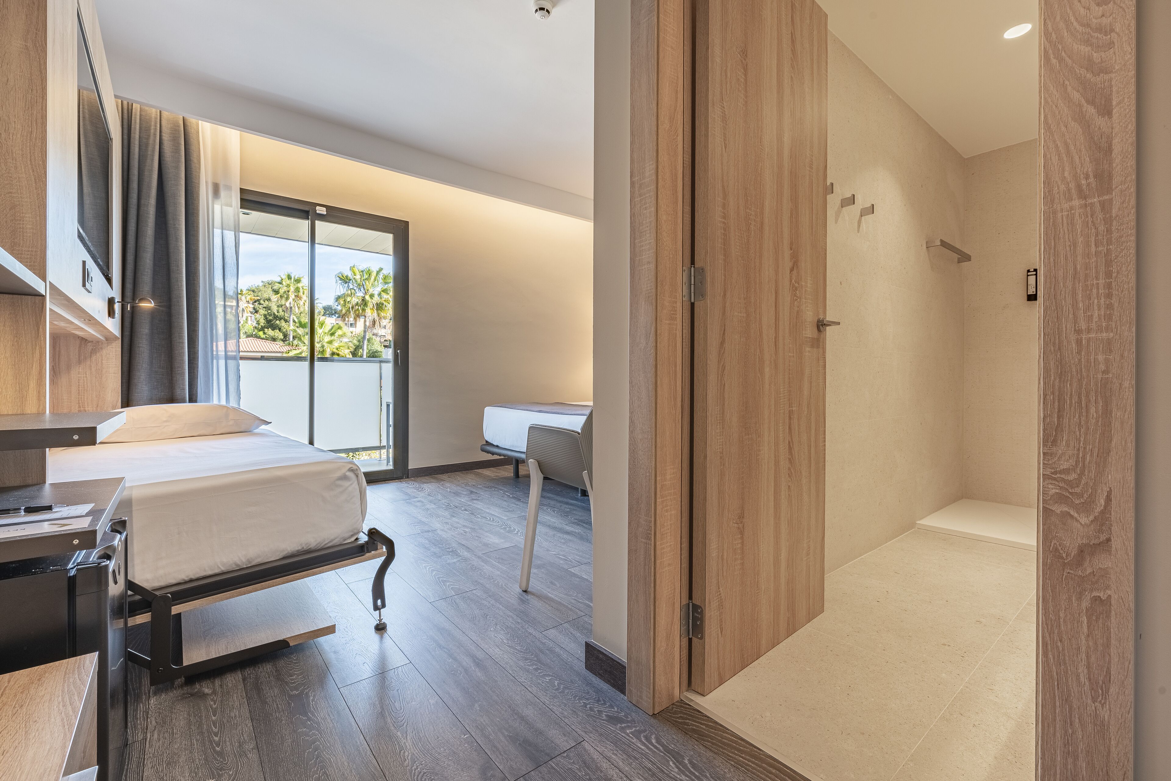 A modern hotel room with a bed, desk, and a shower area.