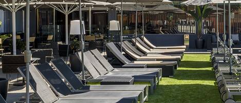 Un espace aménagé au bord de la piscine, avec des chaises longues, des parasols et une piscine.