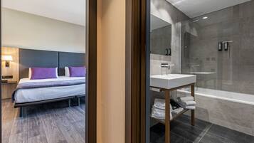 Una habitación de hotel moderna con una cama, una mesita de noche, un baño con ducha, un lavabo y una bañera.