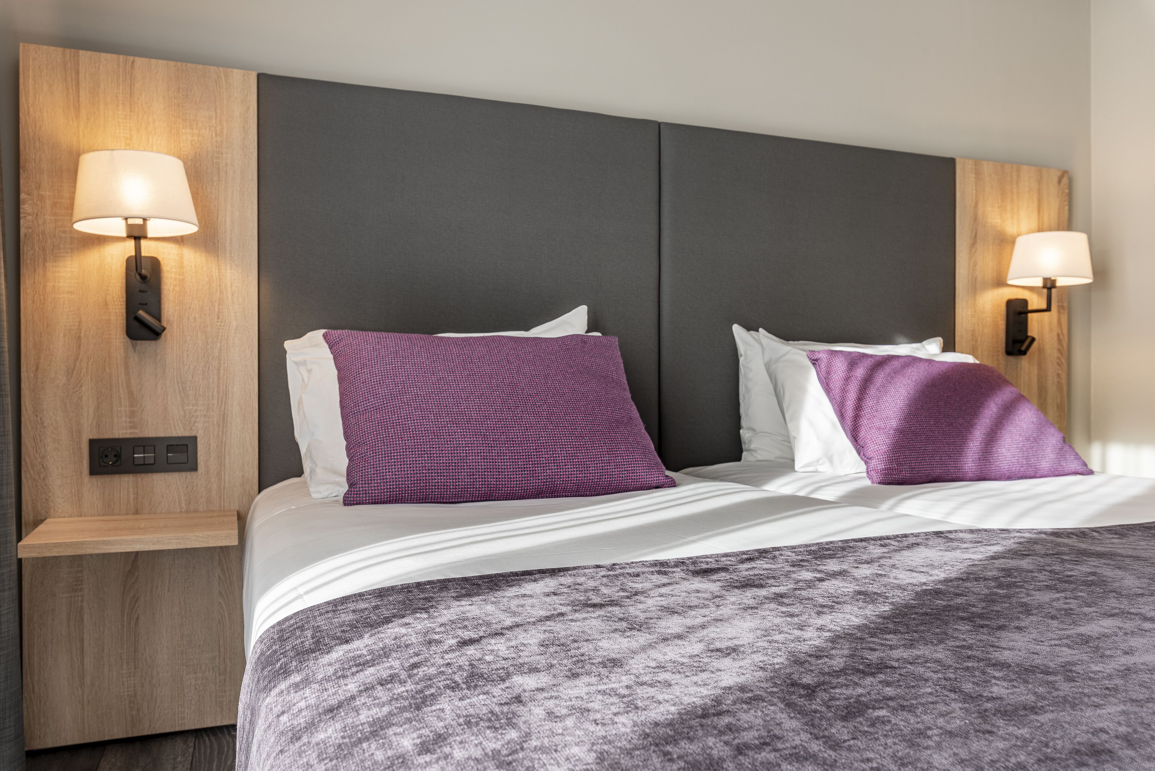 Ein modernes Hotelzimmer mit einem großen Bett, zwei Wandleuchten und einem Nachttisch aus Holz.