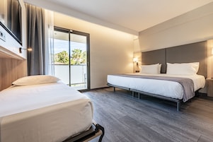 Una camera d'albergo con un letto, un secondo letto, un comodino, una lampada e una porta vetrata scorrevole che dà su un balcone.