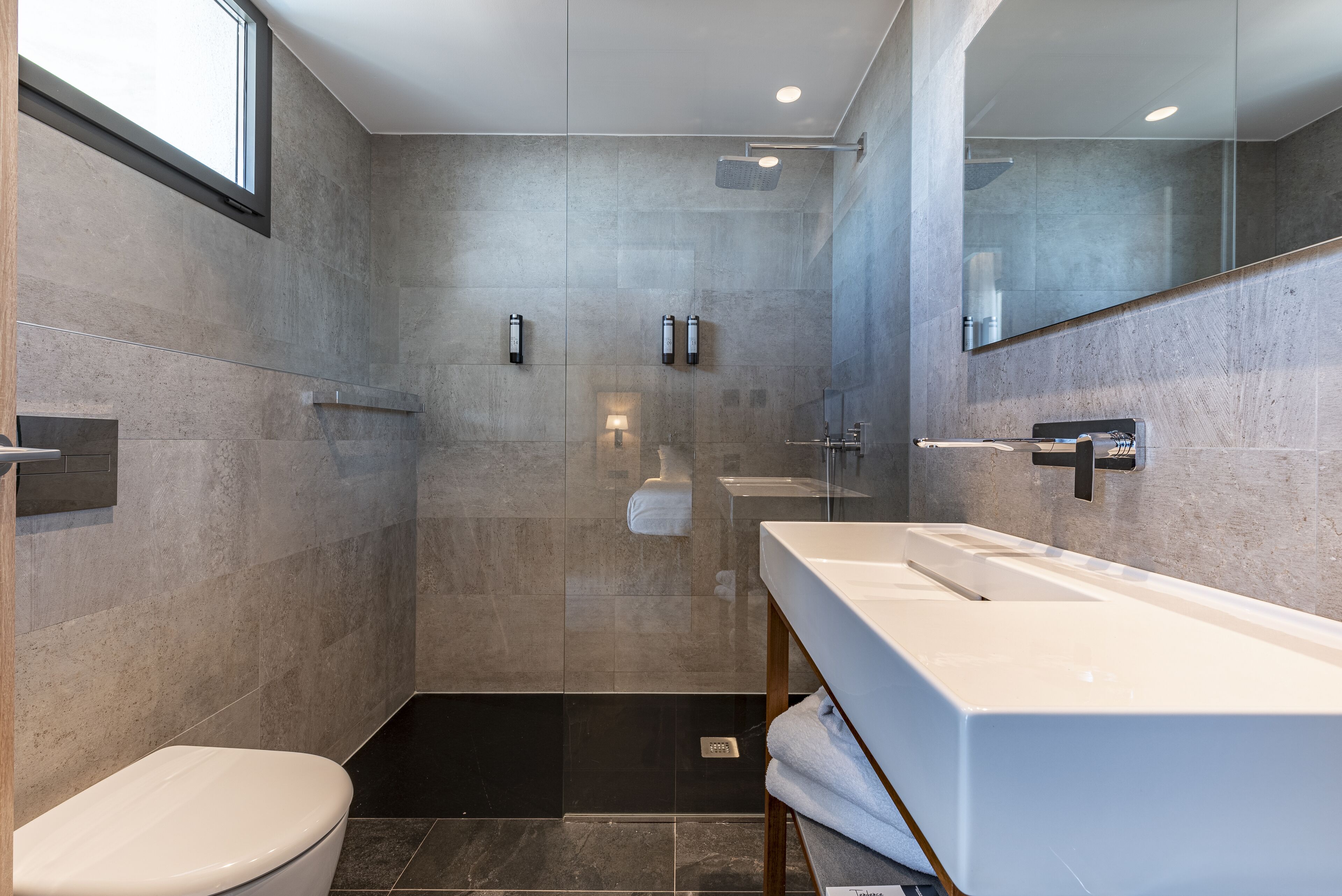 Un baño moderno con un espejo grande, un lavamanos blanco y una zona de ducha.