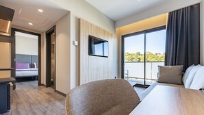 A modern hotel room with a large bed, a desk, a chair, a TV mounted on the wall, and a balcony with a view of greenery. - Hotel Astari (Tarragona)