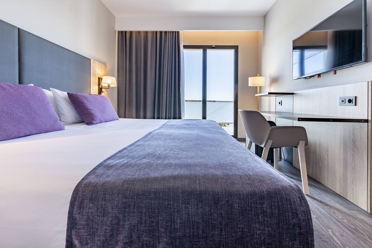 A modern hotel room with a large bed, a desk, and a television.