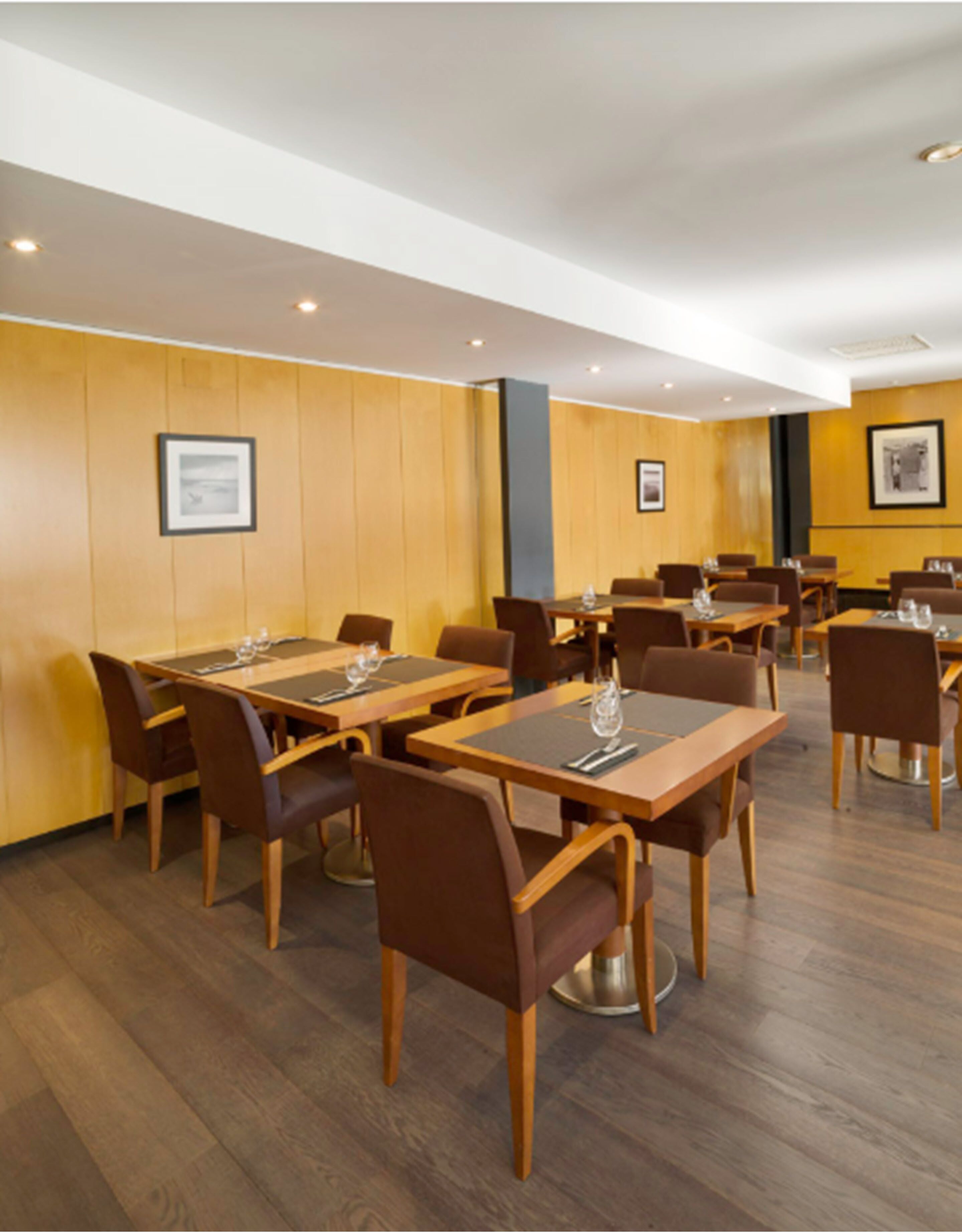 A hotel dining area with multiple tables and chairs, wooden walls, and framed pictures on the walls.