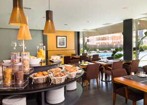 A modern dining area with a buffet setup, including various food items and condiments, and a pool view.