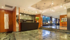 A modern hotel lobby with a reception desk, marble flooring, wooden accents, and pendant lighting. - Hotel Astari (Tarragona)