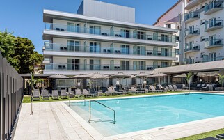 Un hotel moderno con piscina, diversi balconi e aree salotto all'aperto.
