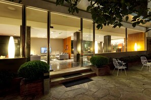 A modern hotel lobby with glass doors, a reception area, and a seating area with chairs and a sofa.
