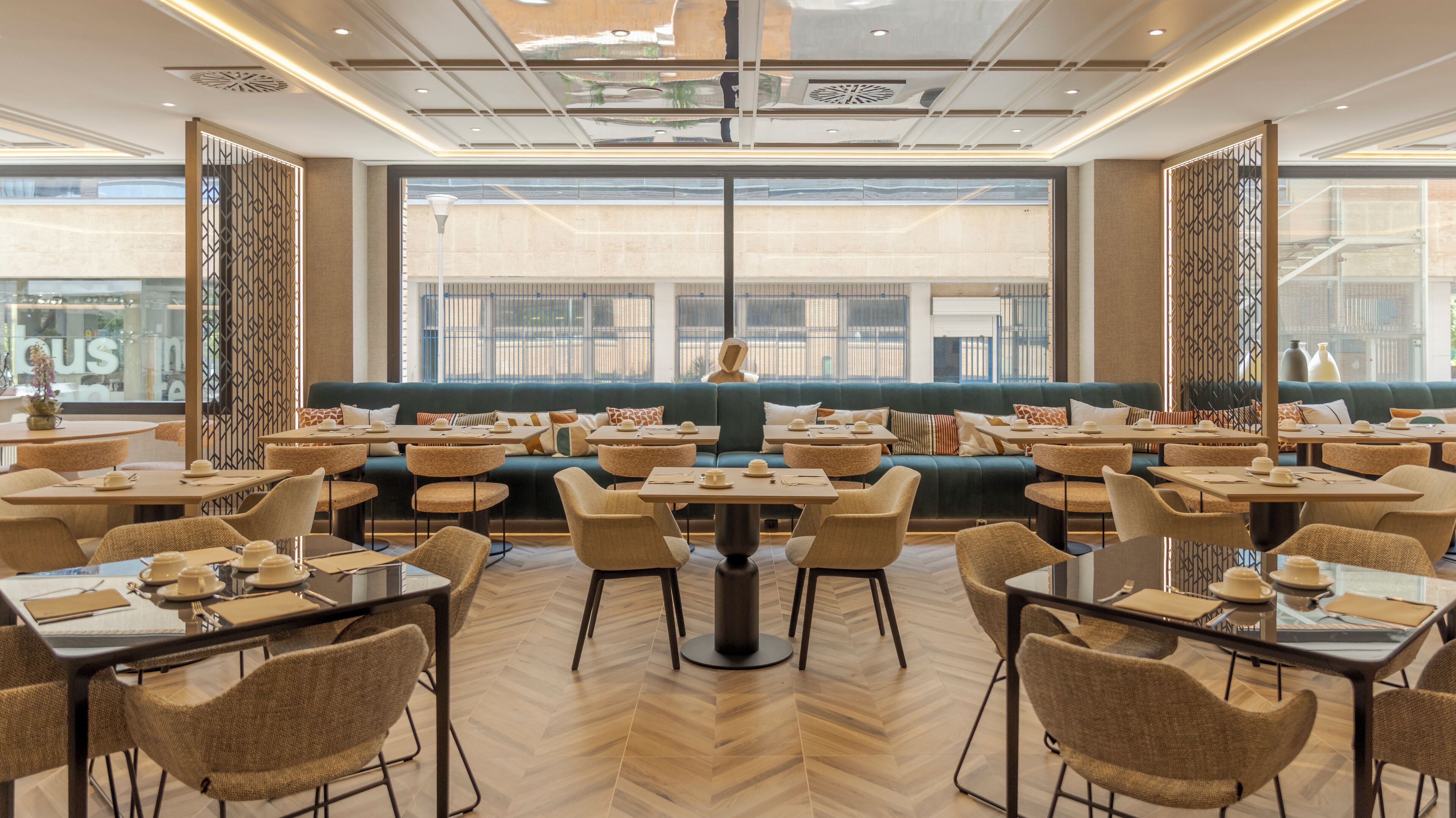 Un comedor moderno con varias mesas y sillas, una zona de estar central con sofás, y grandes ventanales que ofrecen vistas de la ciudad.