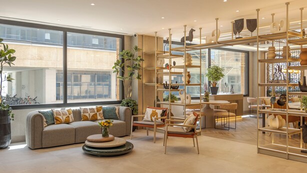 Una sala de estar moderna con un sofá, sillas, una mesita de centro y una estantería decorativa con objetos.