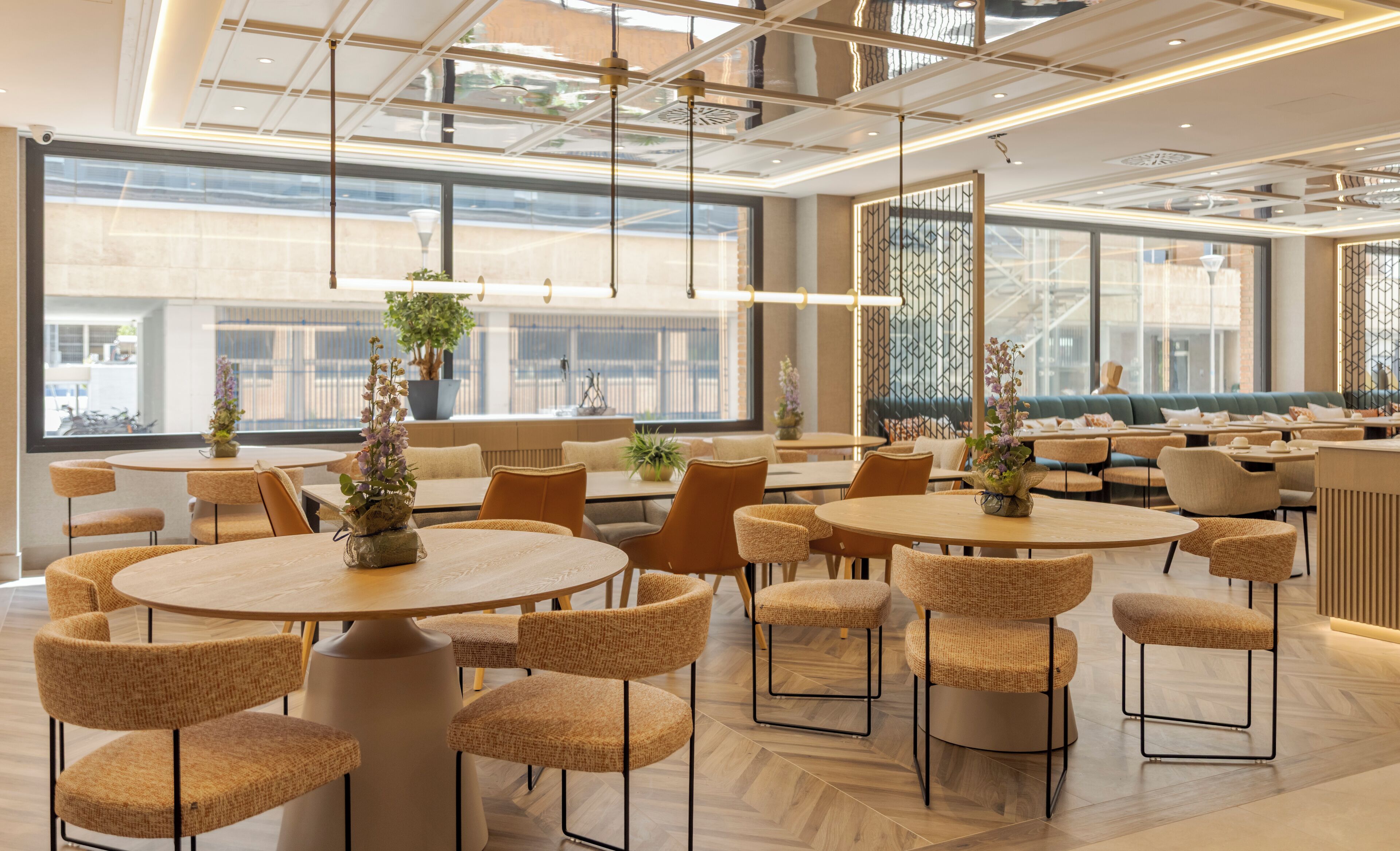 A modern dining area with round tables and wicker chairs, large windows, and hanging pendant lights.