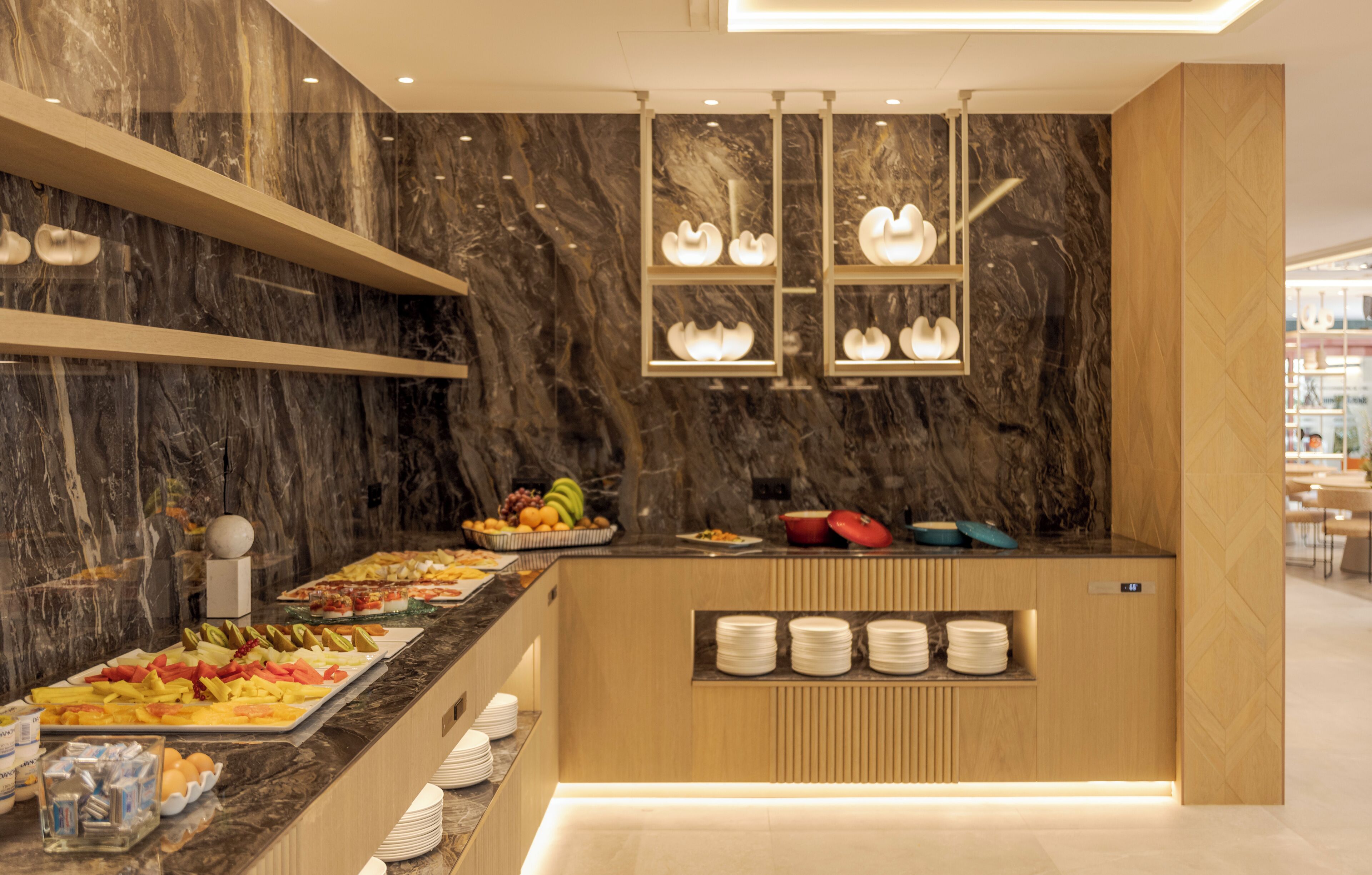 Un moderno montaje tipo buffet con paredes de mármol, diversas opciones de comida y platos ordenados.