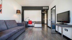 Una sala de estar moderna con un sofá gris, un sillón rojo, un escritorio con una lámpara y un televisor de pantalla plana.