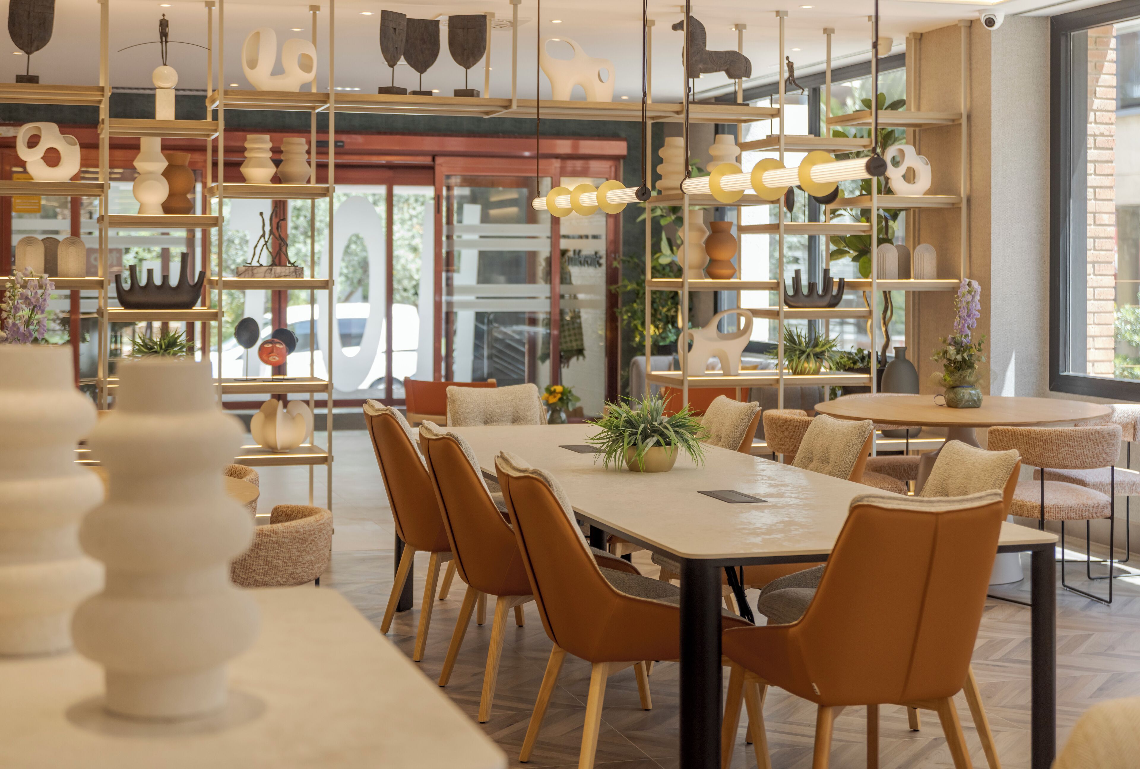 A modern dining area with a large table, multiple chairs, and decorative shelves with various items.