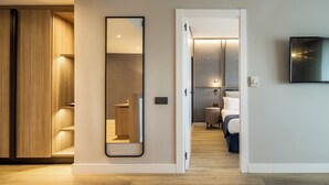 Una habitación de hotel moderna con un armario de madera, un espejo grande, una mesita de noche, una cama y un televisor montado en la pared.