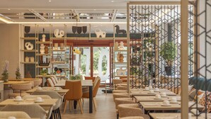 Un restaurante moderno con diversas opciones de asientos, como mesas y cabinas. Se observan estantes con objetos decorativos y plantas.